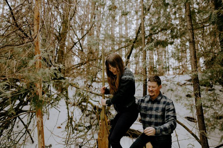 innisfil Engagement photography of couple climbing through a deep wintery forest together