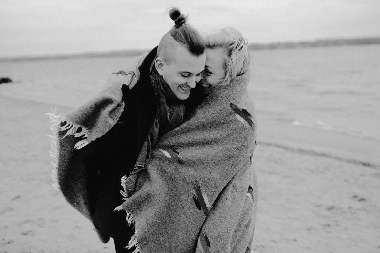 barrie Ontario engagement photography of couple walking together on the beach wrapped in a blanket laughing