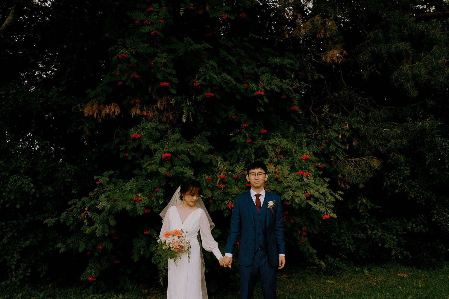 Brockville Ontario Wedding photography of bride and groom holding hands in front of deep green foliage