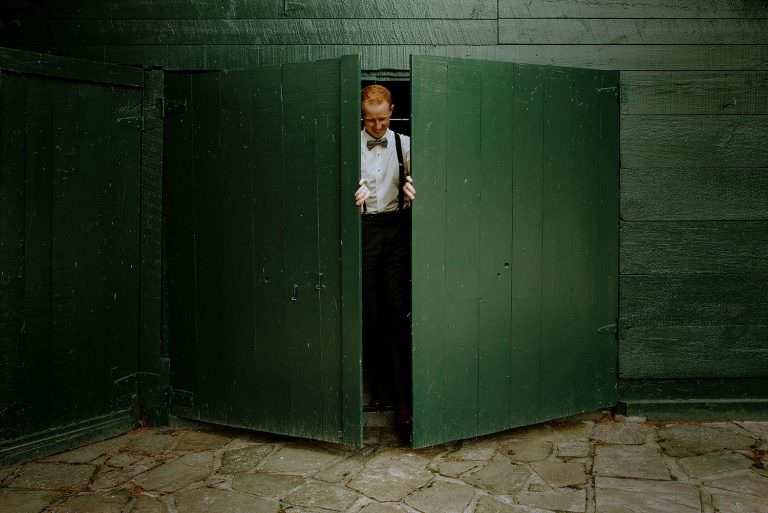 groom exits green door during a wedding photography session on Manitoulin islands in McGregor Bay