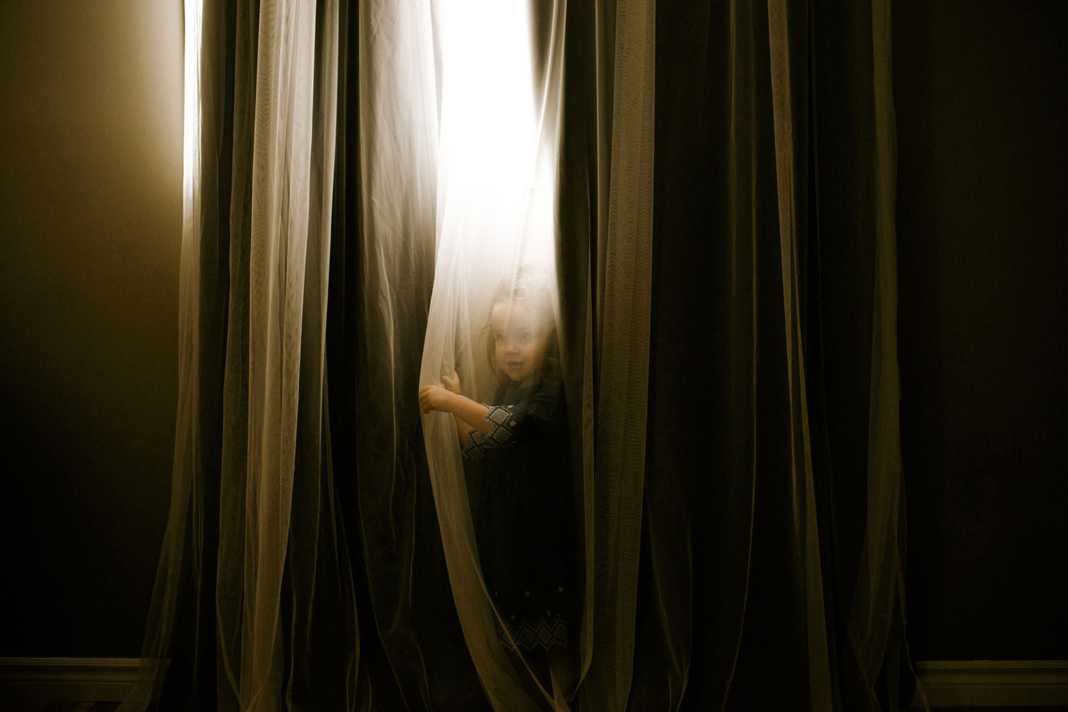 little girl hiding behind sheer curtains for a family photography shoot in sudbury Ontario