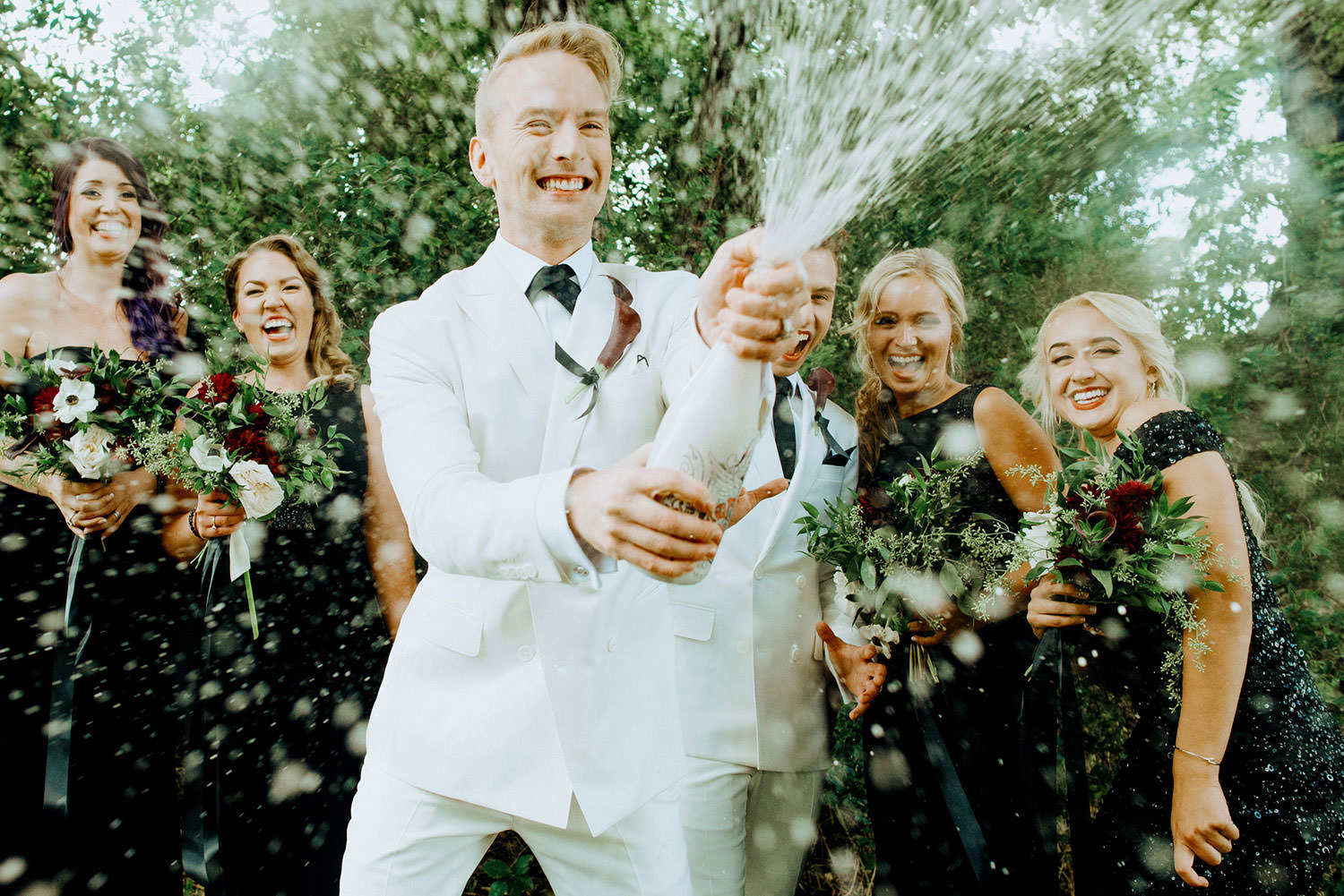 groom sprays champagne while wedding party laughs during a wedding photography session in Niagara on the lake