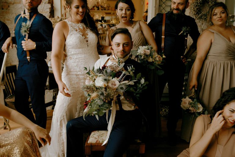 Sudbury Ontario Wedding photography of groom holding the bouquet elegantly as the bridal party laughs candidly behind him