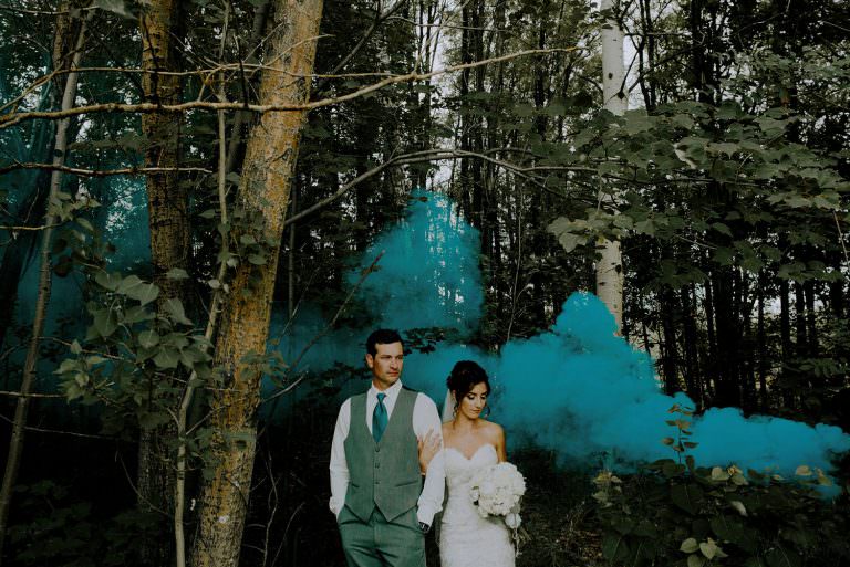 Sudbury Ontario Caruso Club Wedding photography of bride and groom standing in deep forest with blue smoke bomb going off in the background