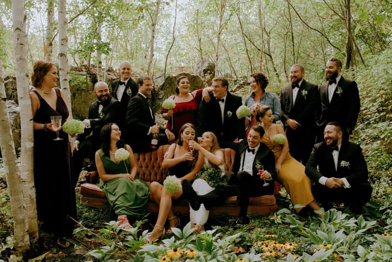 sudbury Ontario wedding photography of a bridal party candidly laughing outside together on a vintage couch in the forest