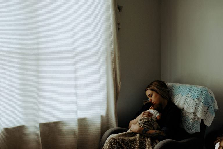 newborn photography in Sudbury Ontario of mom holding new baby in chair by the window