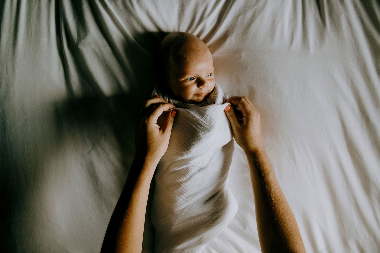 Sudbury Ontario lively newborn photography of baby being swaddled on a bed with a smile on his face