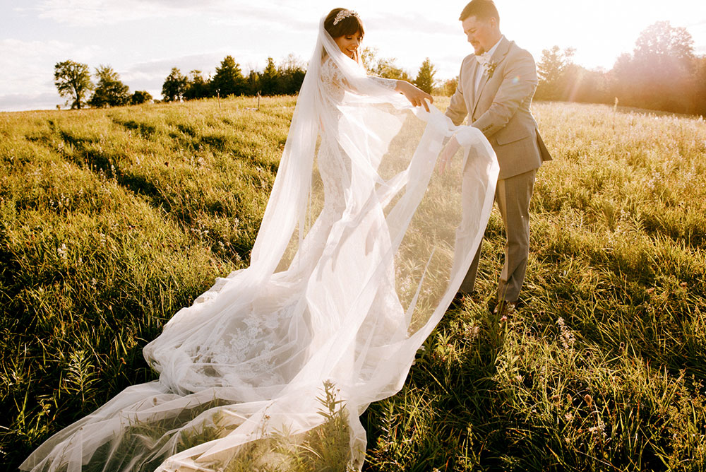 bride and groom play with a long veil during their portrait session at golden hour in rolling hills by the heritage view barn