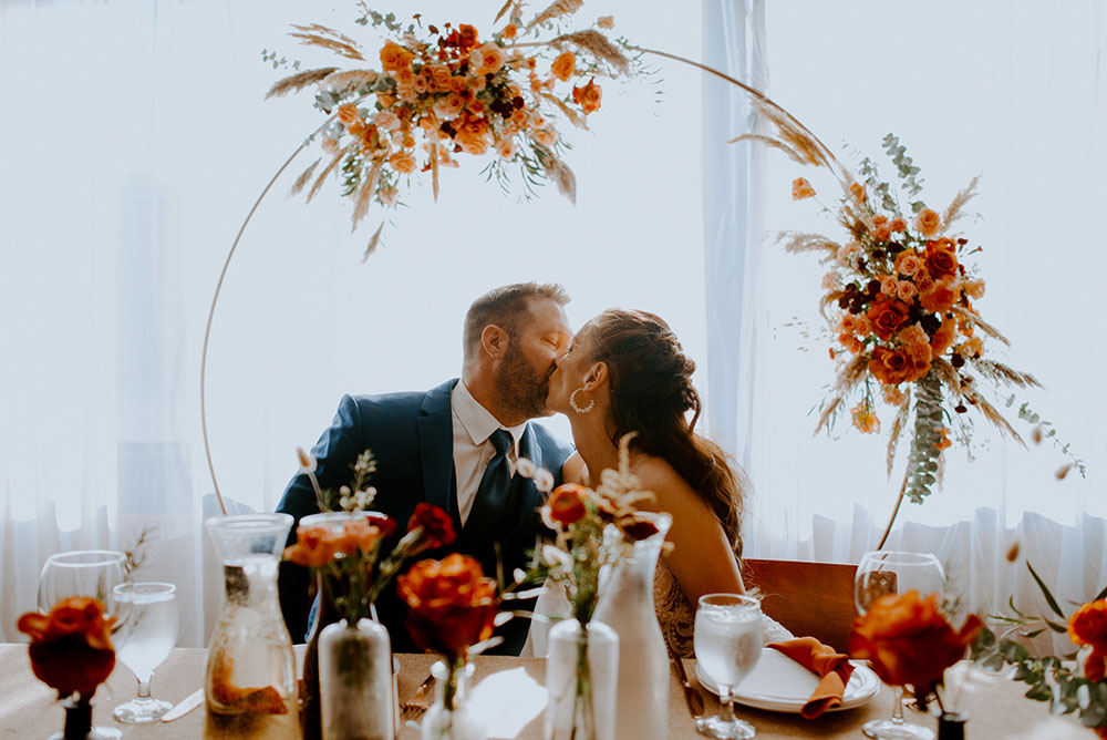 couple kiss at the head table at their wedding reception held at respect is burning kitchen in sudbury surrounded by decor by inspire design studio in toronto