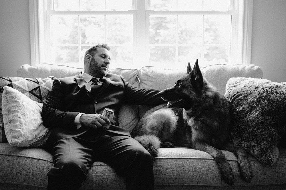 groom sits on the couch with his dog & a beer on the morning of his wedding