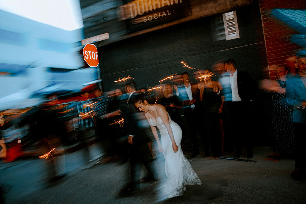 Blurry shot of wedding guests with sparklers in the alley way beside respect is burning kitchen