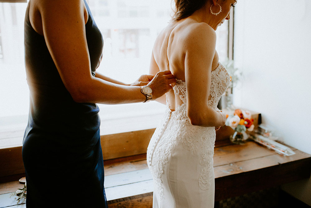 bride getting her gown buttoned up by maid of honour