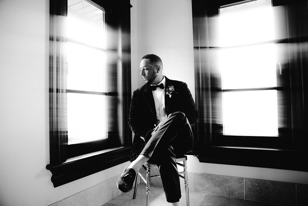 groom looks out window as he awaits the ceremony at the Catana Estate