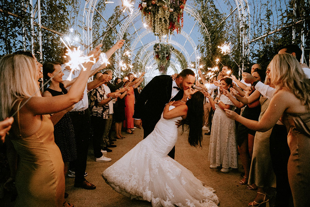 groom dips his bride for a kiss sourounded by guests with sparklers at the Catana Estate