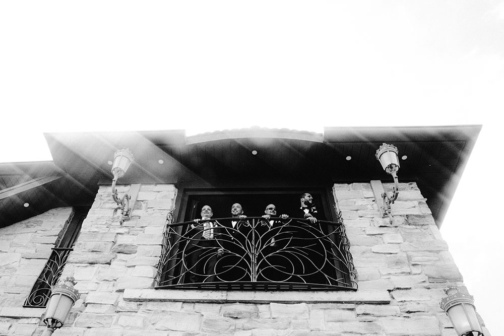 groomsmen stand at the window overlooking the grounds at the Catana Estate