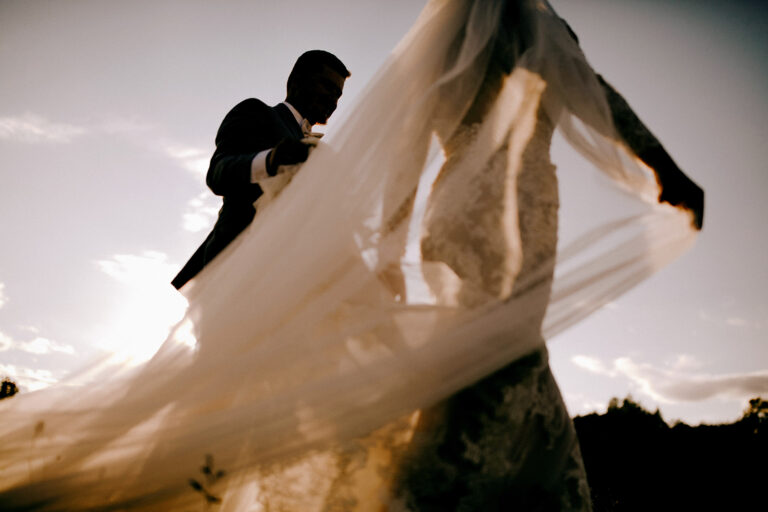 bride's stunning veil trails behind in the wind as she walks with her groom outdoors