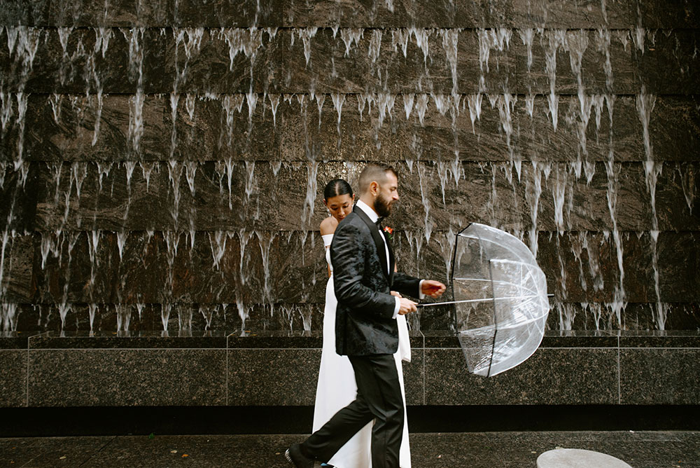 Sassafraz Yorkville Wedding Photography of the wedding couple posing candidly in front of a water wall attached to the Four Seasons in Yorkville