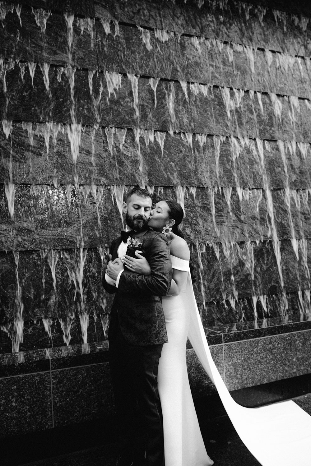 Sassafraz Yorkville Wedding Photography of the wedding couple posing candidly in front of a water wall attached to the Four Seasons in Yorkville