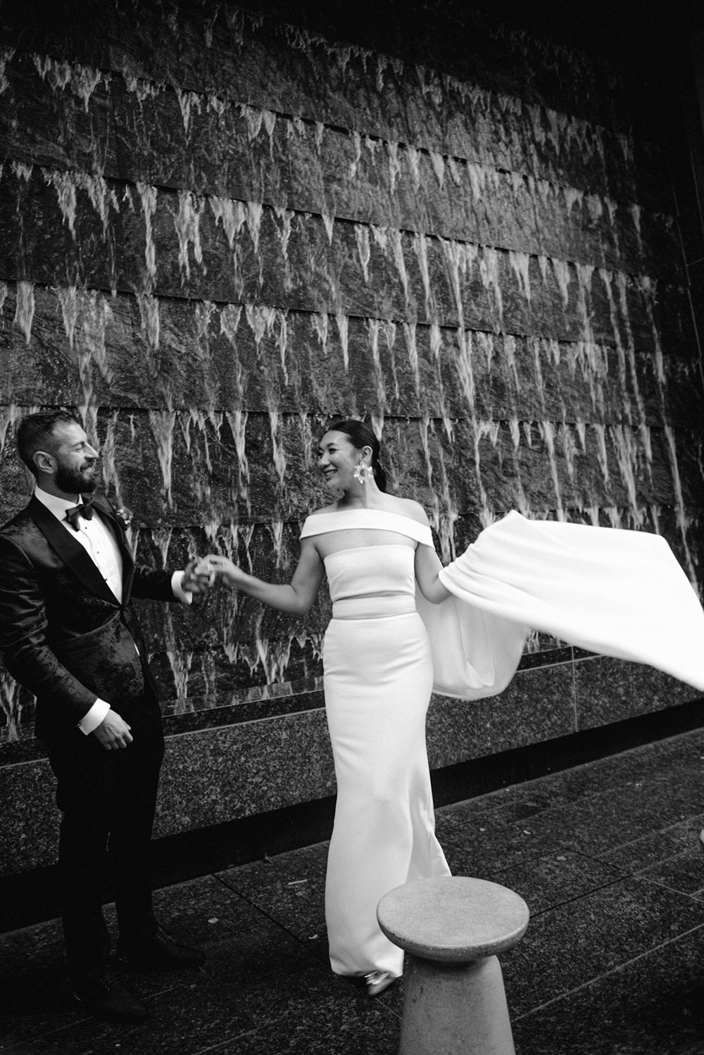 Sassafraz Yorkville Wedding Photography of the wedding couple posing candidly in front of a water wall attached to the Four Seasons in Yorkville