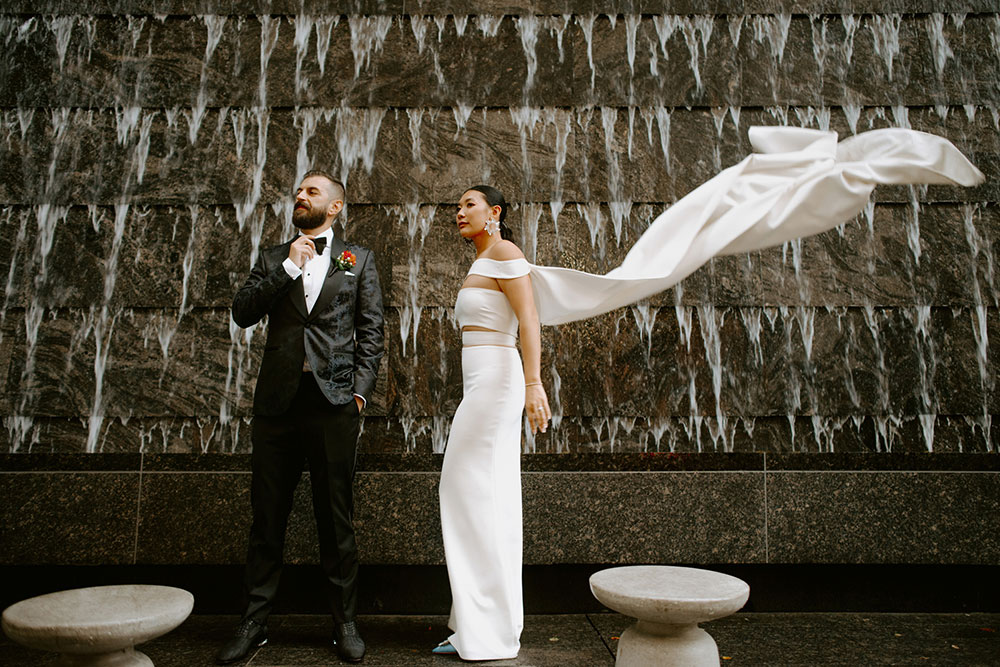 Sassafraz Yorkville Wedding Photography of the wedding couple posing candidly in front of a water wall attached to the Four Seasons in Yorkville