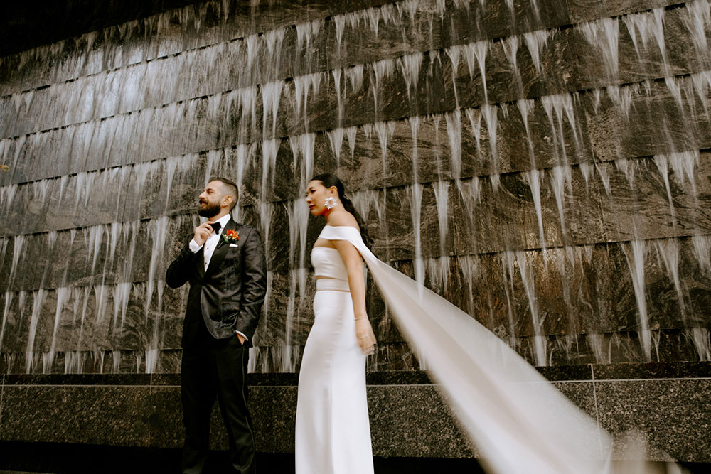 Sassafraz Yorkville Wedding Photography of the wedding couple posing candidly in front of a water wall attached to the Four Seasons in Yorkville