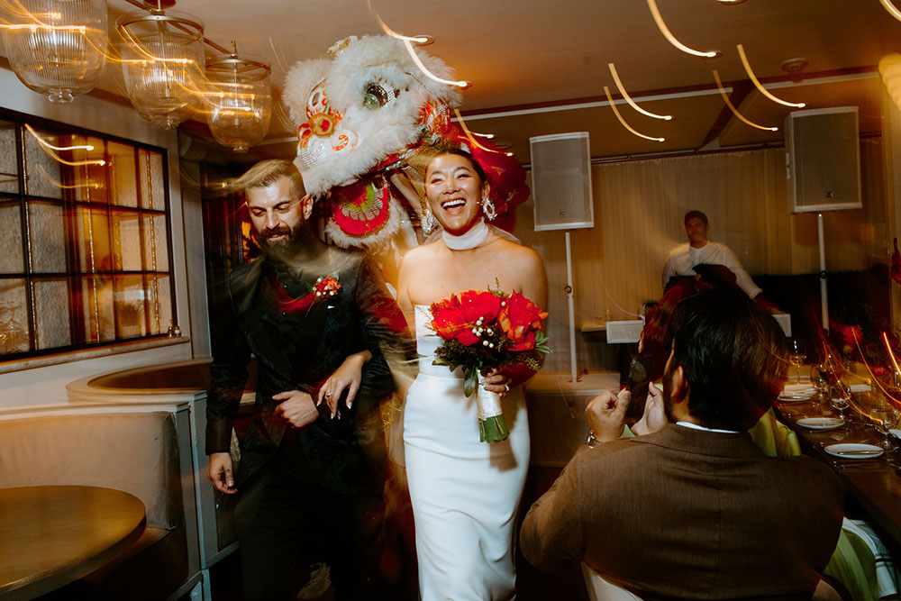 Sassafraz Yorkville Wedding Photography of the wedding couple walking into the wedding reception followed by lion dancers