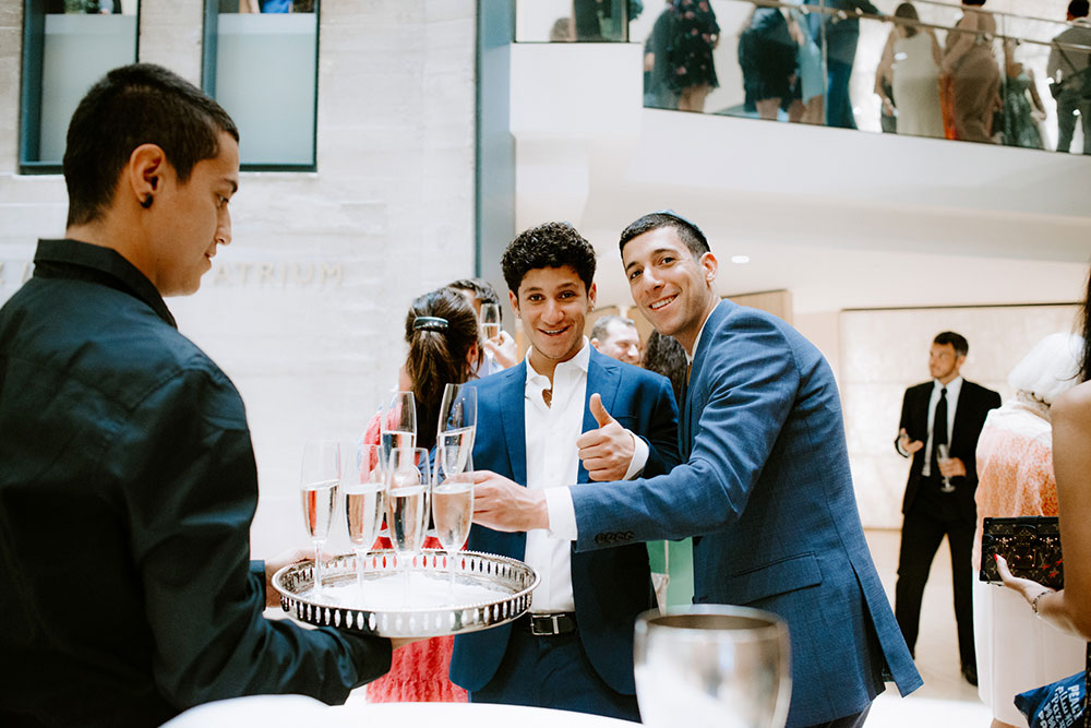 Young men take a glass of champagne from a server at a cocktail hour 