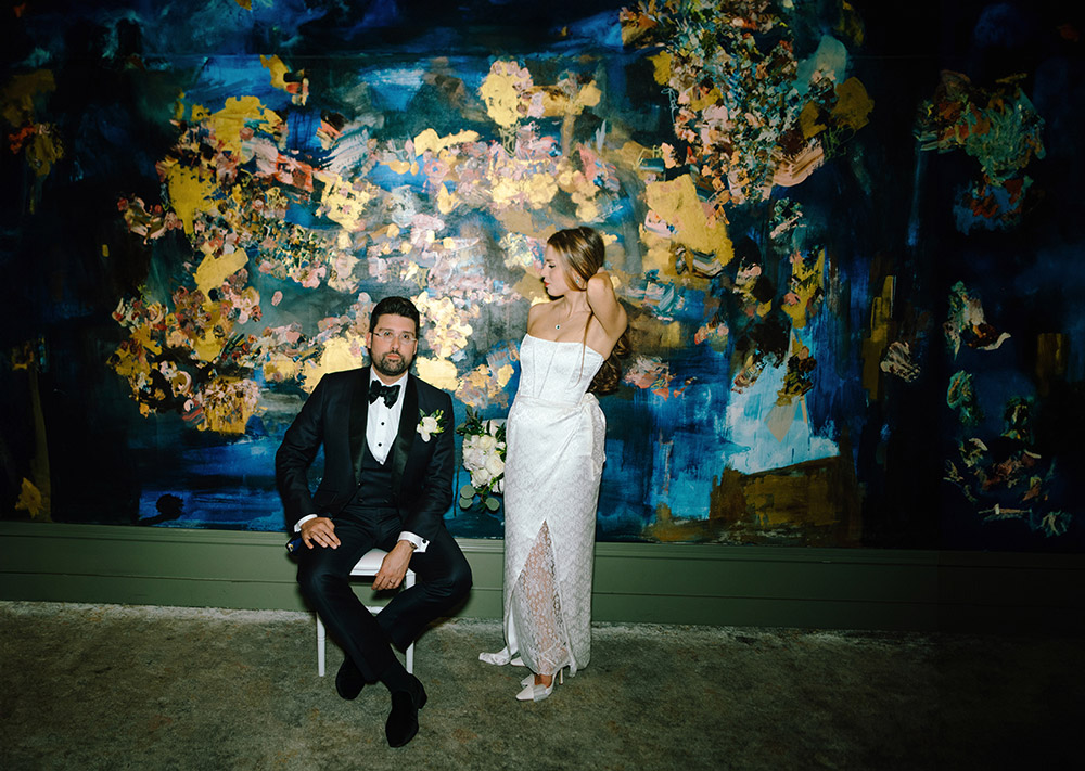 Bride and groom pose for a photo in front of giant canvas painting in the ceremony room during their Antonio Park wedding in Toronto 