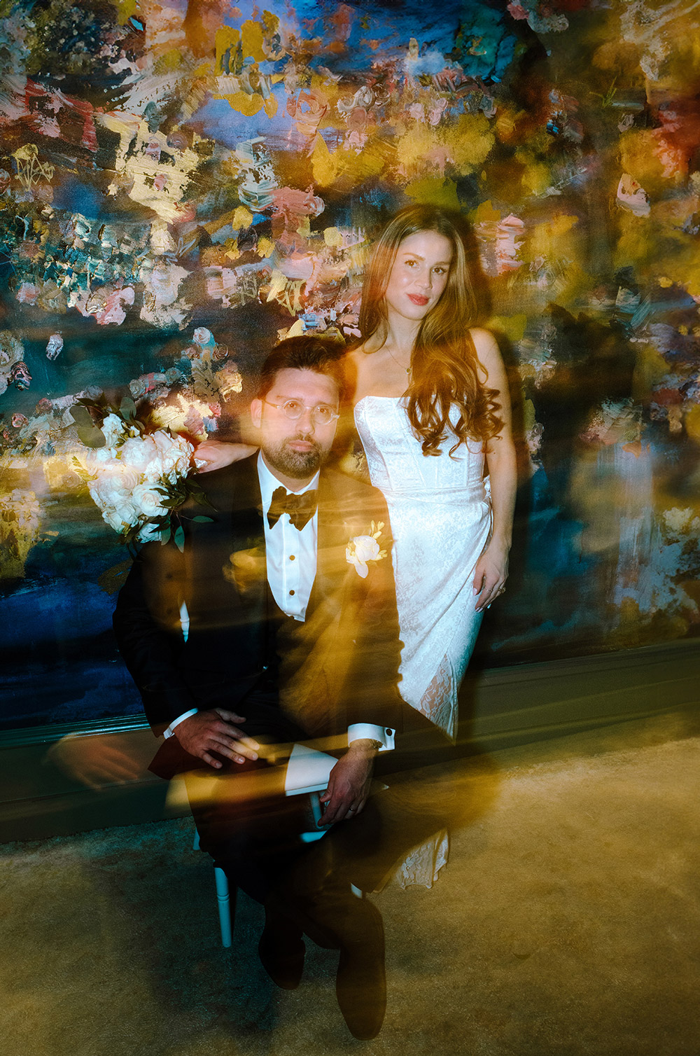 Bride and groom pose for a photo in front of giant canvas painting in the ceremony room during their Antonio Park wedding in Toronto 