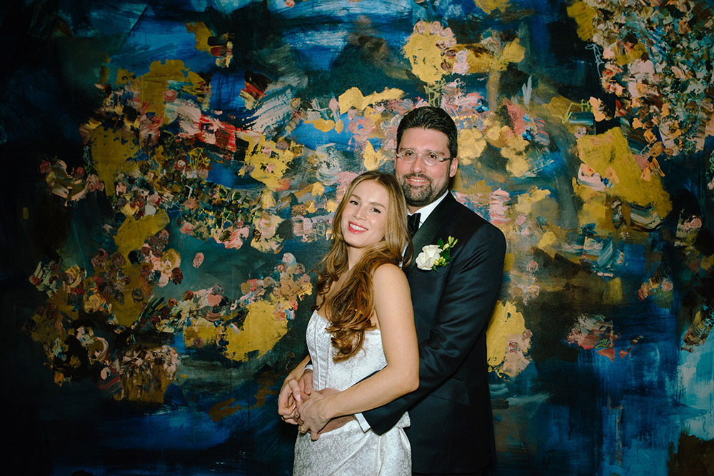 Bride and groom pose for a photo in front of giant canvas painting in the ceremony room during their Antonio Park wedding in Toronto 