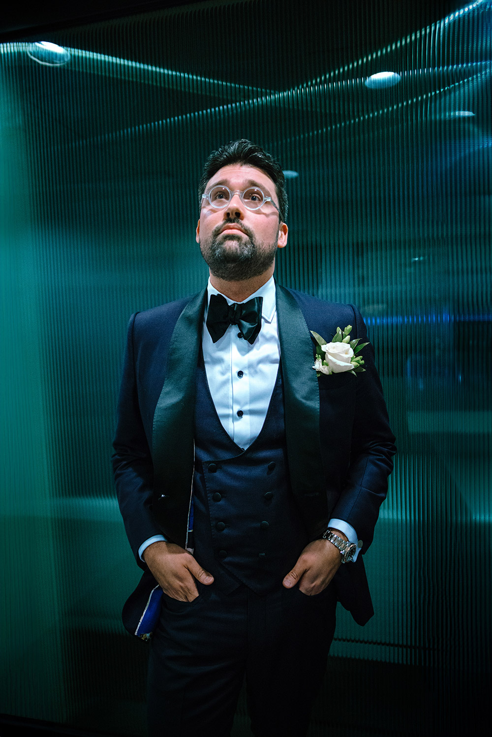 Groom poses in front of ribbed glass wall on his wedding day