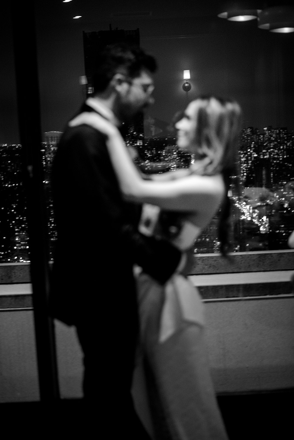 a blurry photo of a bride and groom focusing on the city scape behind them at the top of the manulife centre in Toronto's Yorkville at their Antonio Park wedding