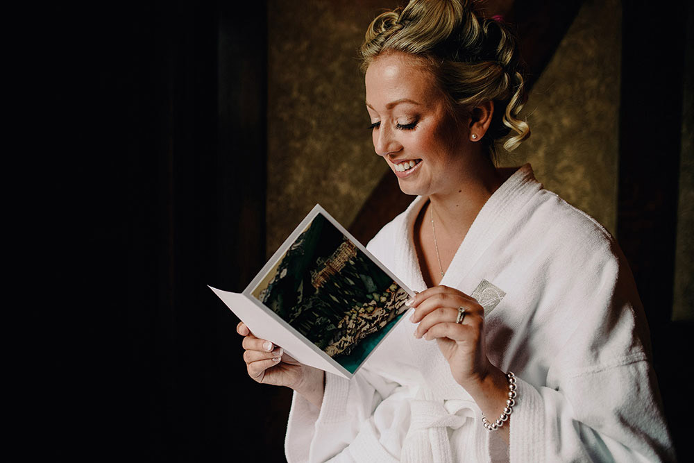Bride sits in her robe reading a card with a smile on her face at this Banff Fairmont Wedding