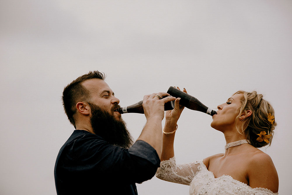 couple seal their vows with a much deserved drink of belkin beer at the top of a mountain in the jungle at this belize adventure wedding