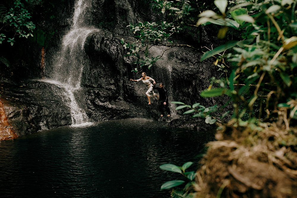 couple jump from the waterfall in their wedding clothes in the jungle at this belize adventure wedding