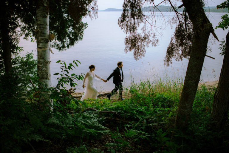 Northridge Inn Wedding Photographer Captures bridge & groom walking along the shoreline of a very calm lake in Muskoka