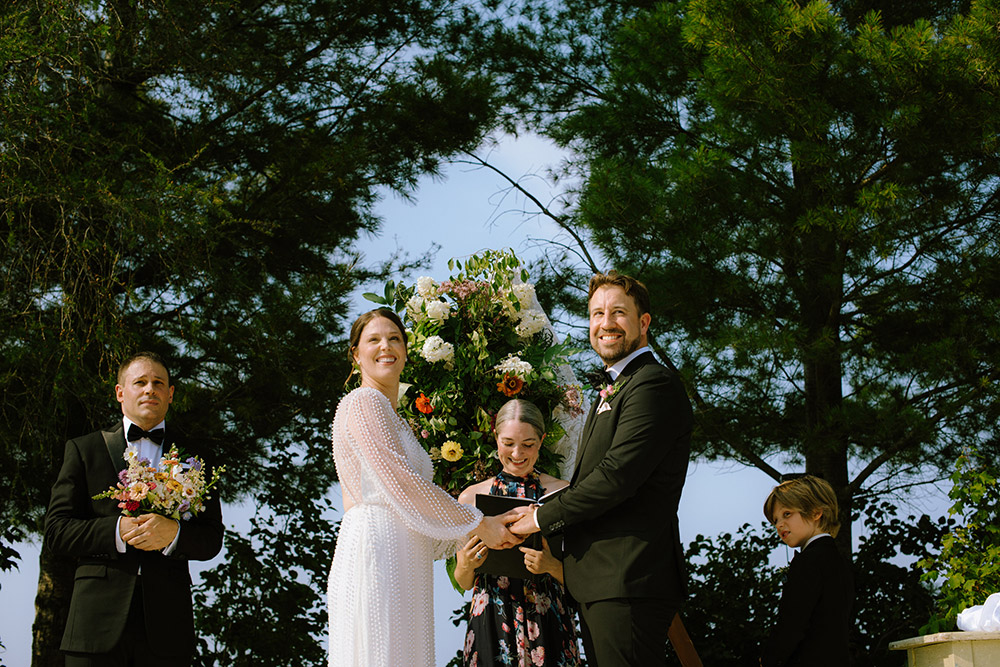 Bride and groom hold hands and look off to the crowd as they enjoy the final moments of their wedding ceremony on the dock at the Northridge Inn Resort located in Muskoka Ontario