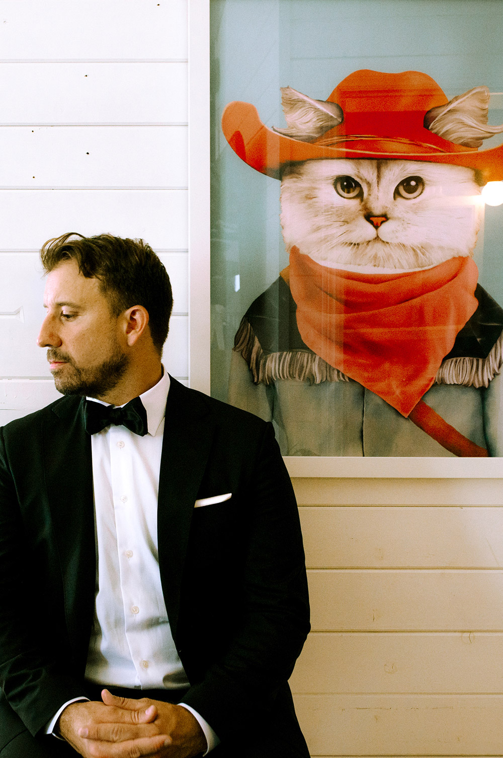 Groom poses beside a print of cowboy cat just before his wedding ceremony at the Northridge Inn in Muskoka