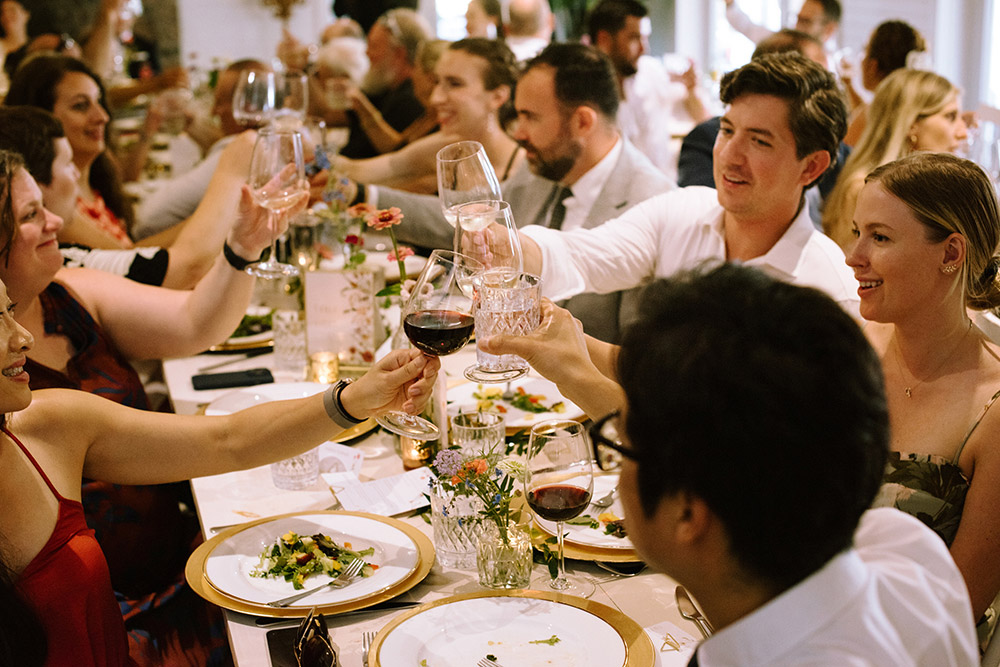 Guests all cheers with various drinks at a wedding dinner table during speeches at a muskoka wedding held at the Northridge inn resort