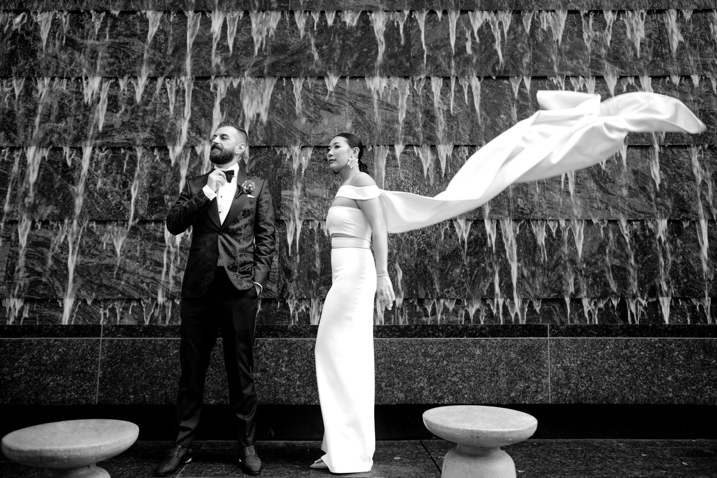 Toronto Wedding Photography of Wedding Couple posing very elegantly in front of the Four Seasons in Yorkville Downtown Toronto while the bride's Wedding Gown flies in the windy weather