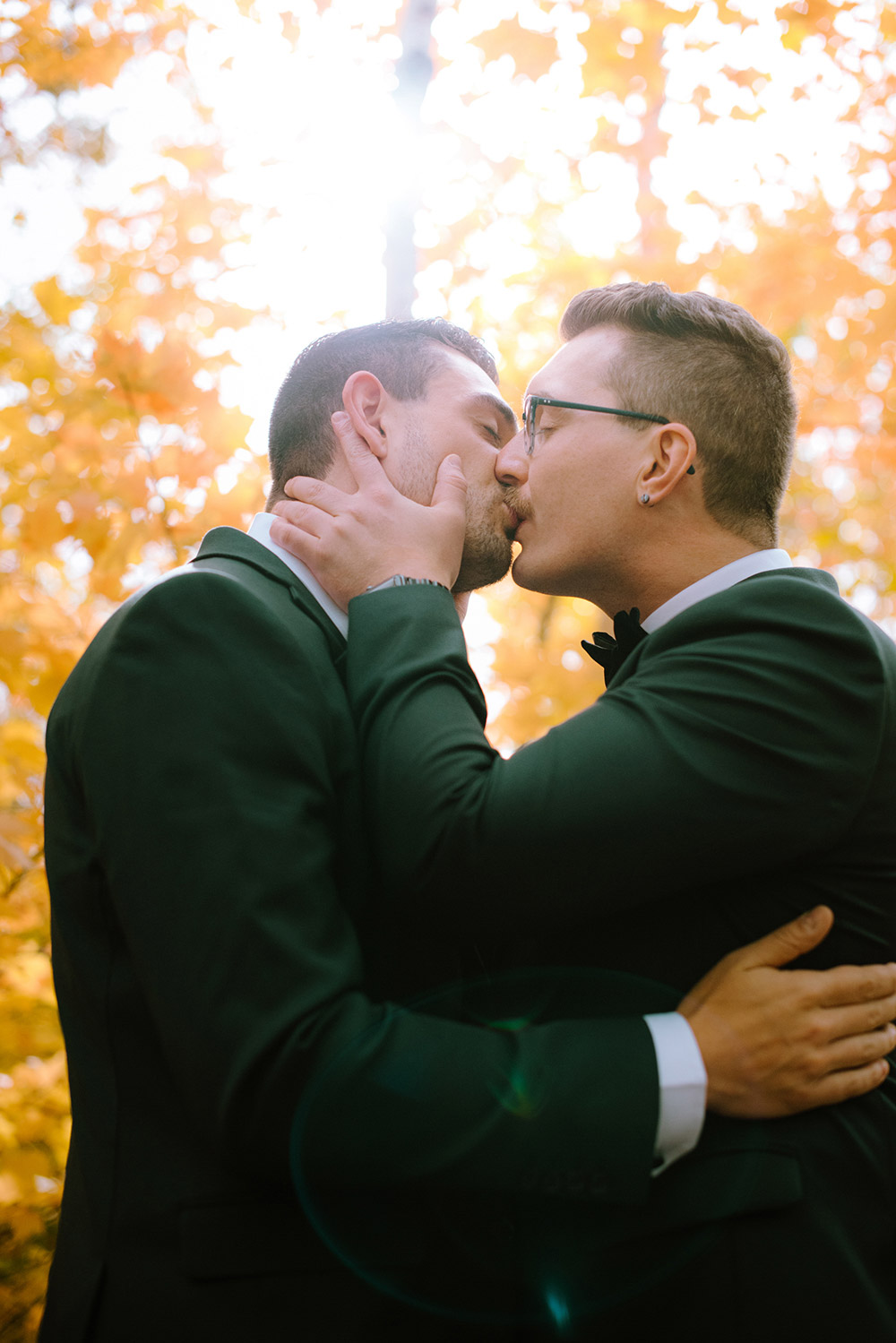 grooms kiss under the fall leaves moments before they get married at this science north wedding