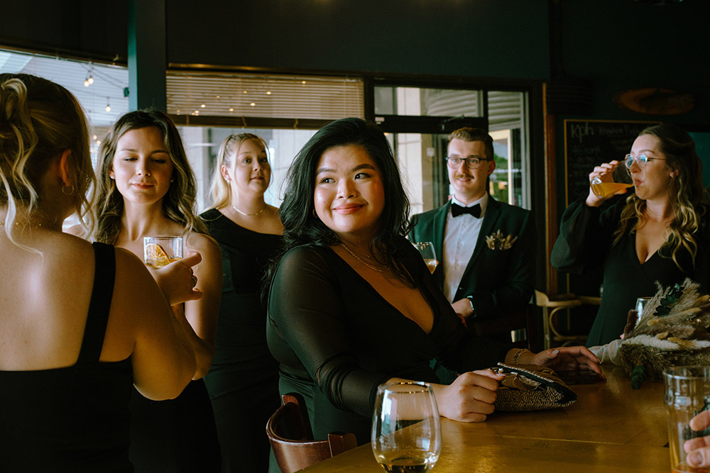 bridesmaid smiles taking a moment to enjoy the happy for her grooms while standing at the bar