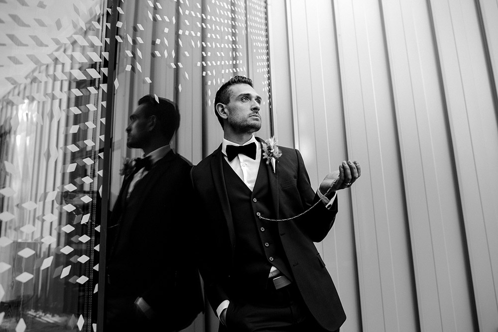 groom poses against buidling while holding his pocket watch at his science north wedding