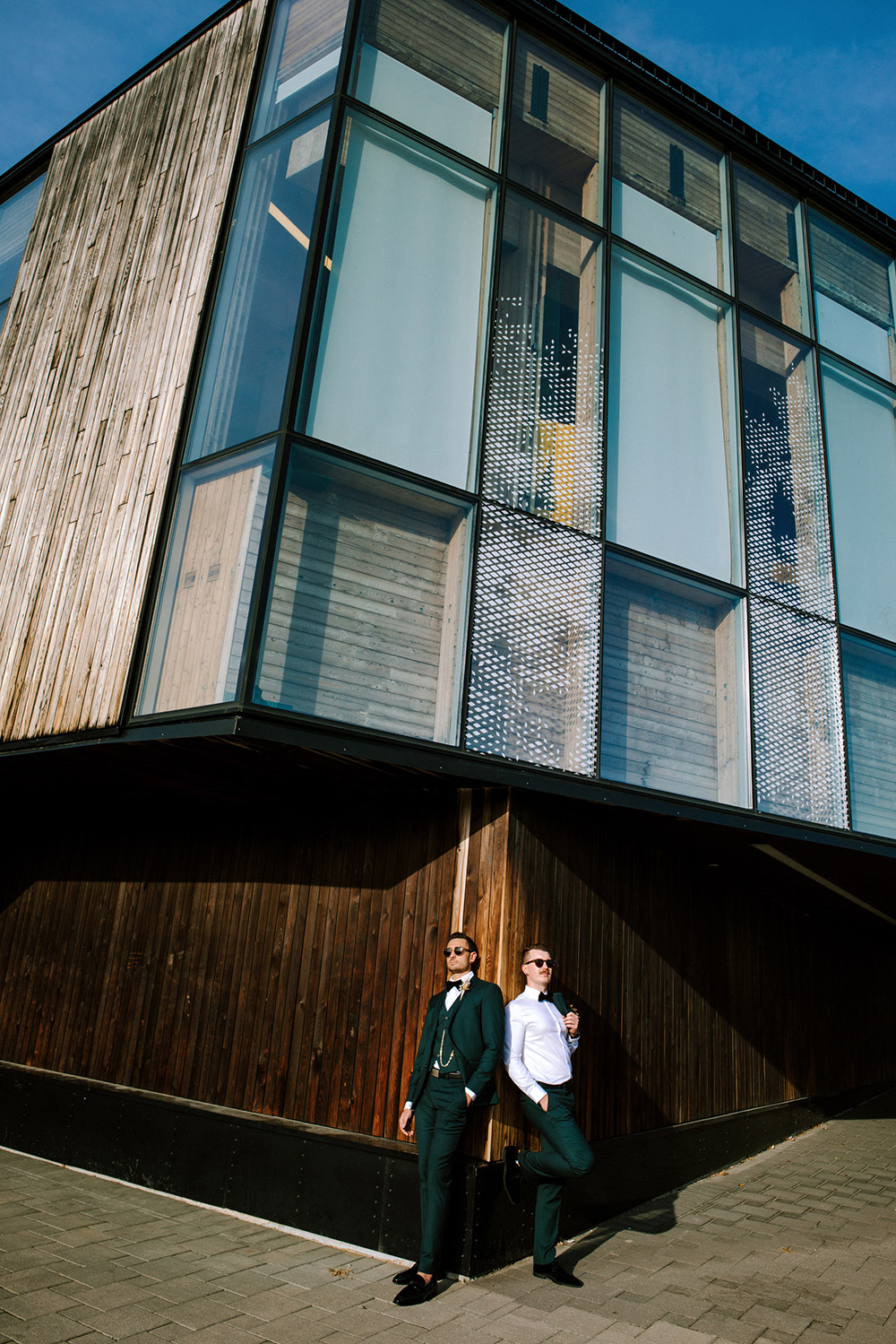 wide photo of grooms posing against building on a sunny day for their science north wedding