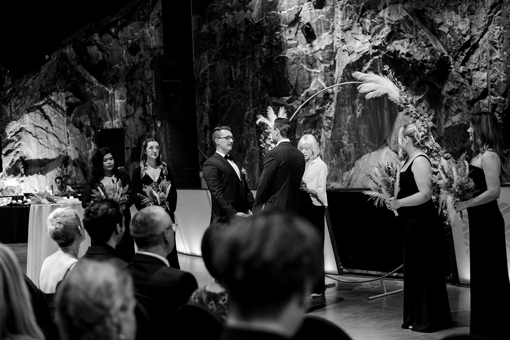 grooms hold hands during the ceremony held in the cavern at this science north wedding