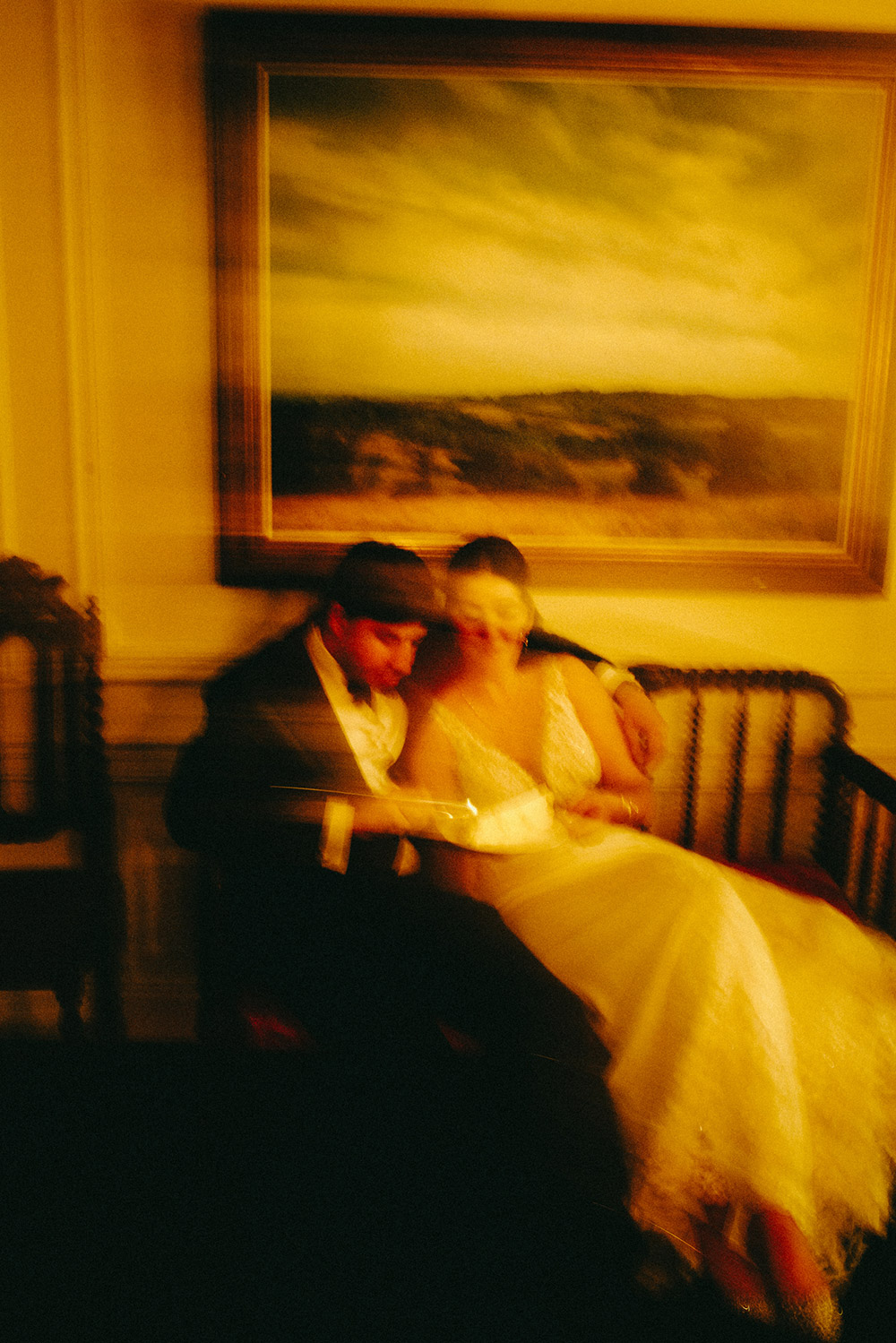 artsy blurry shot of a wedding couple sitting on a bench in front of a large painting at The Doctor's House Wedding