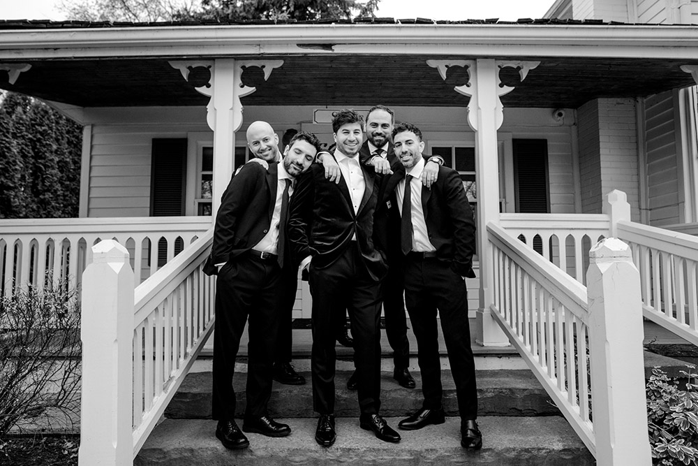 groomsmen pose for a group photo on the steps of one of the cottages at The Doctor's House Wedding