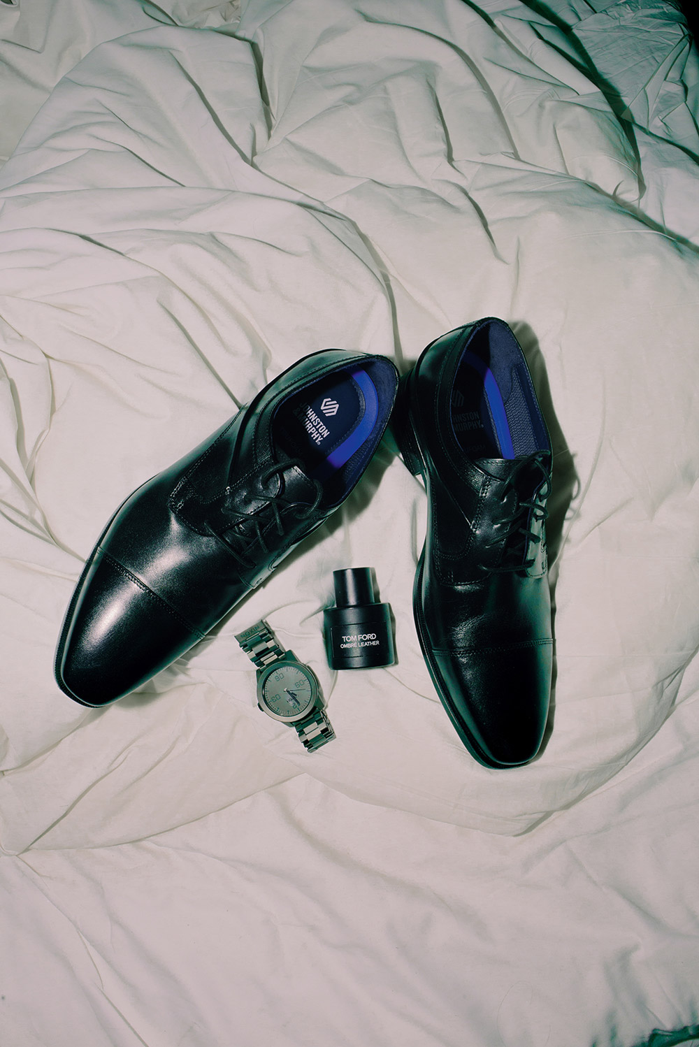 flash photo of mens shoes, cologne and watch on white sheet
